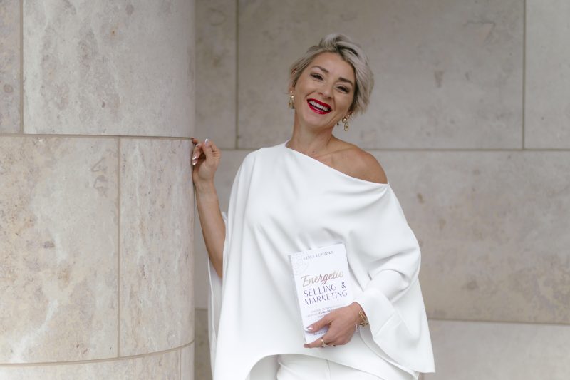 Lenka Lutonska, founder of Business Energetics®, in a camel trench coat and brown tailored outfit, outdoor editorial portrait for Brand You Magazine